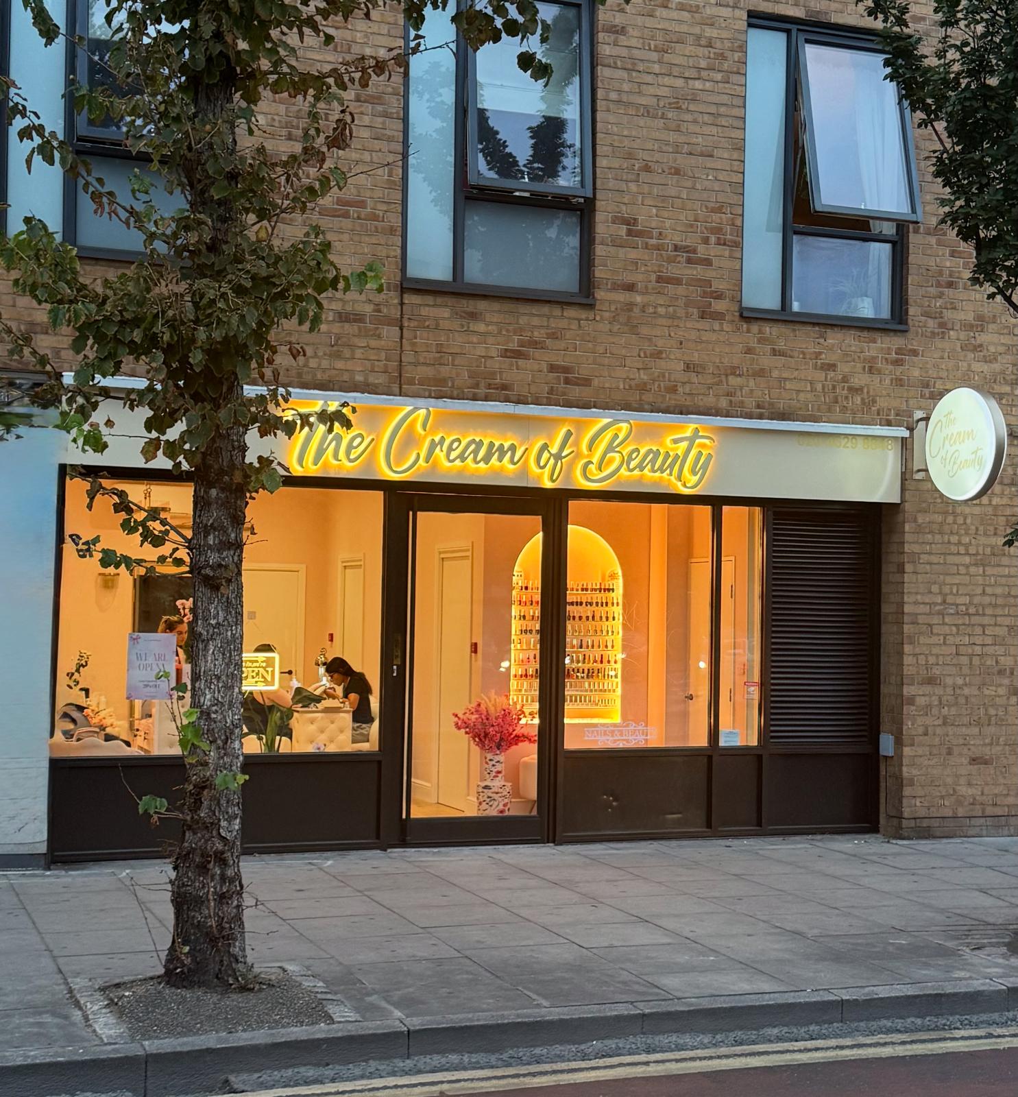 The Cream of Beauty salon storefront in Hackney, London with warm glowing neon sign